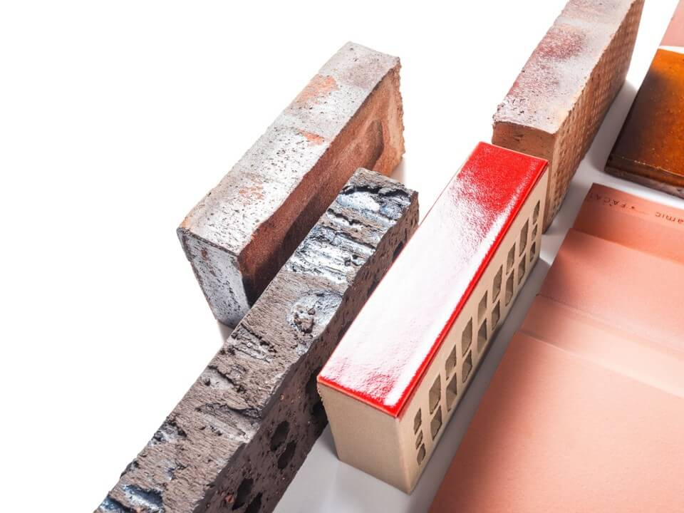 A studio composition displaying a variety of bricks with distinct textures, colors, and finishes—including glazed, rough, and traditional clay surfaces—highlighting the range of materials architects consider for precise and expressive brick design.